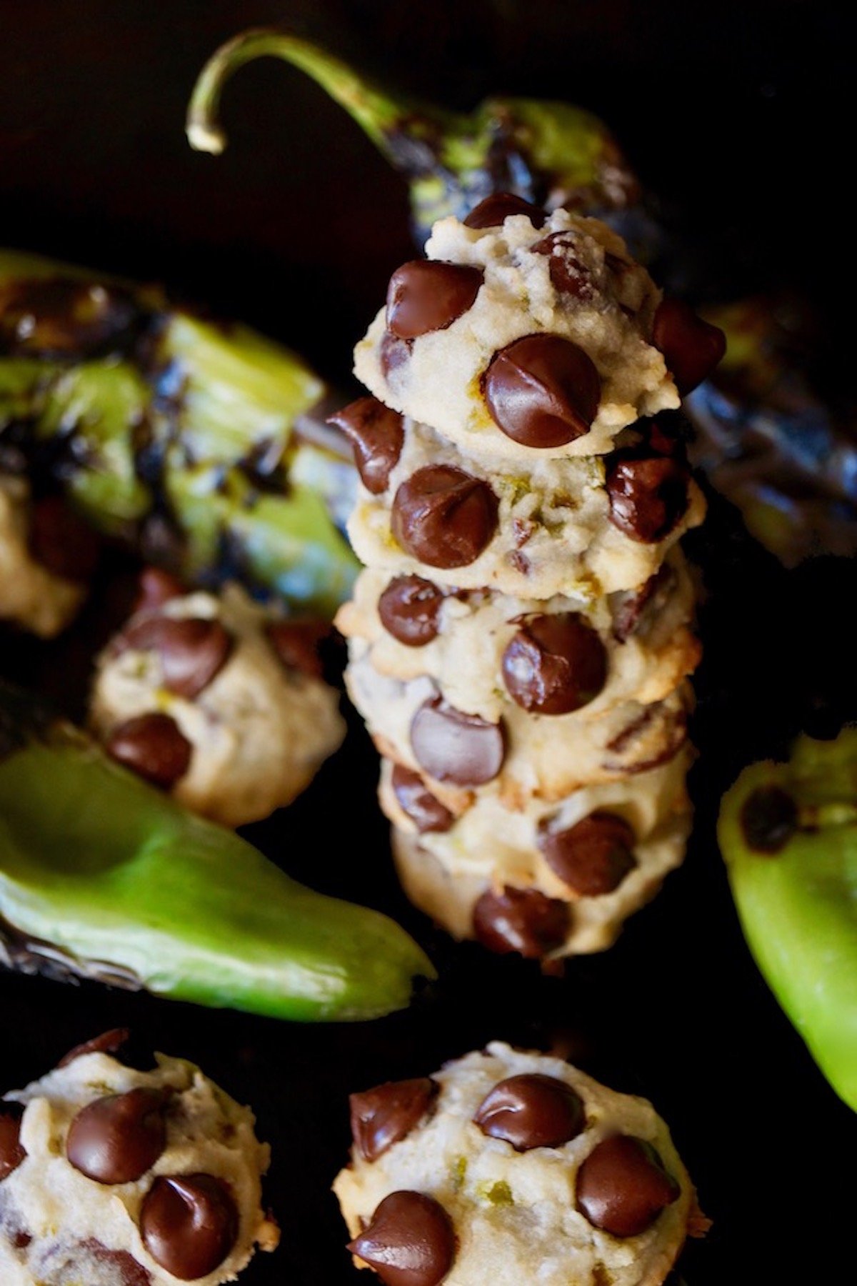 Tall stack of 5 Hatch Chile Chocolate Chip Cookies surrounded by roasted Hatch chiles.
