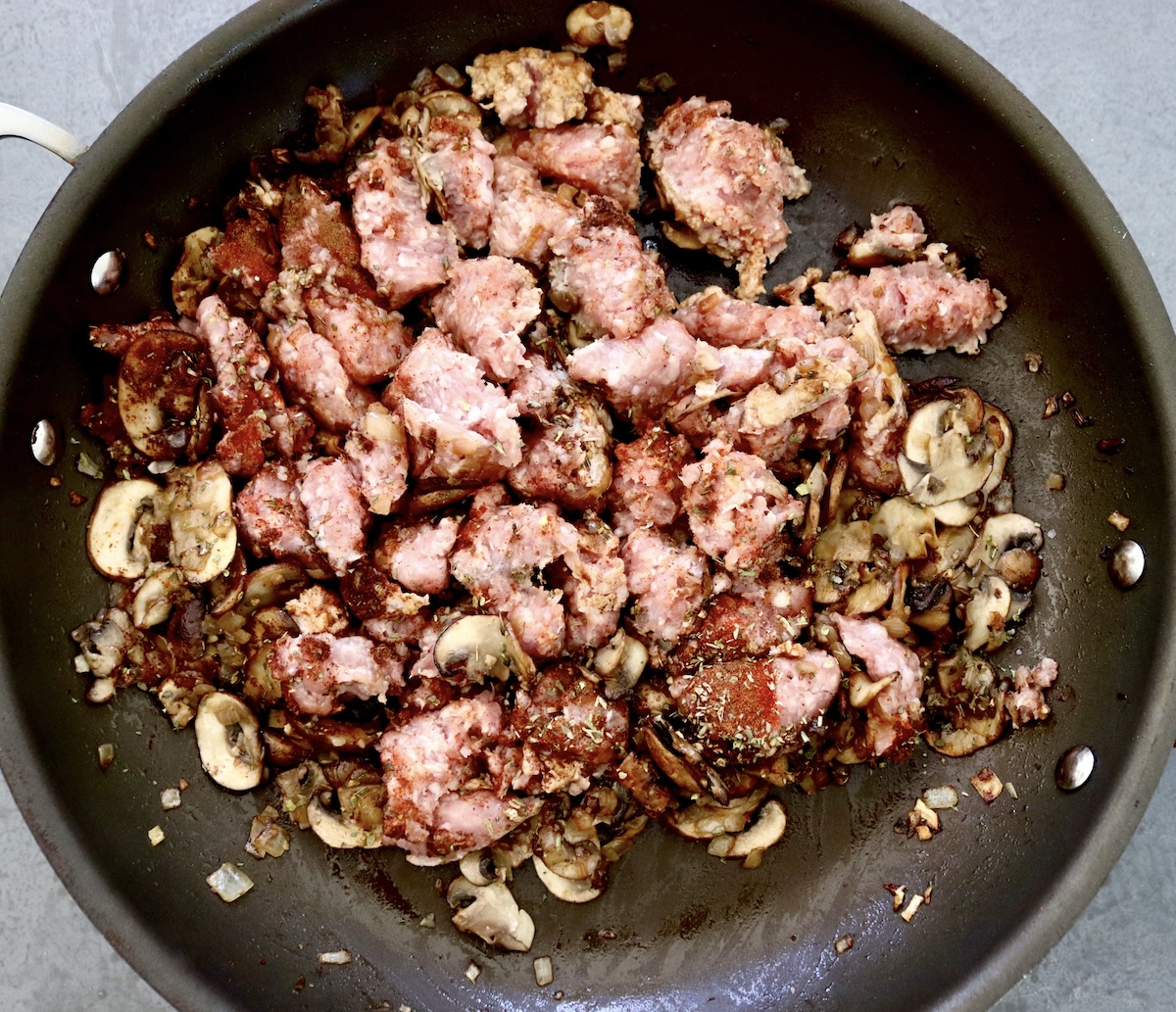 Portuguese-Style Sausage-with-Mushrooms Raw pork, cooked mushroom slices and onion in a skillet.