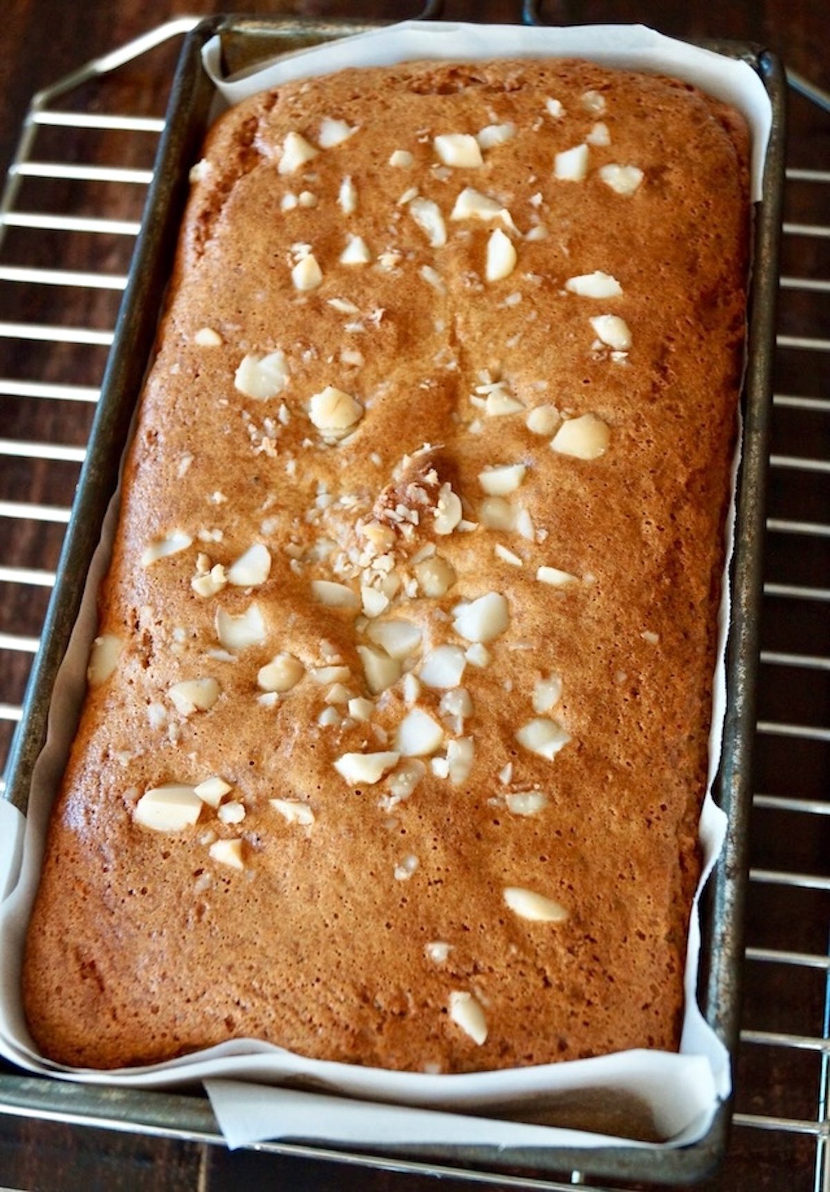 Baked golden loaf of macadamia nut bread in a loaf pan on a cooling rack.