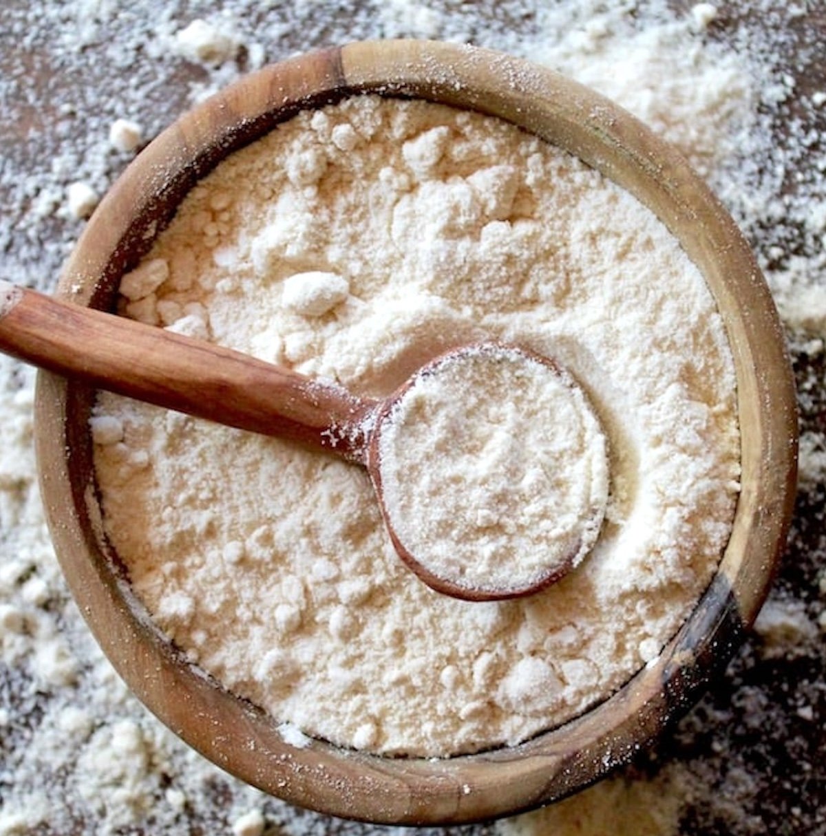 Wooden bowl filled with coconut flour with a small wooden spoon, and coconut flour sprinkled around it.