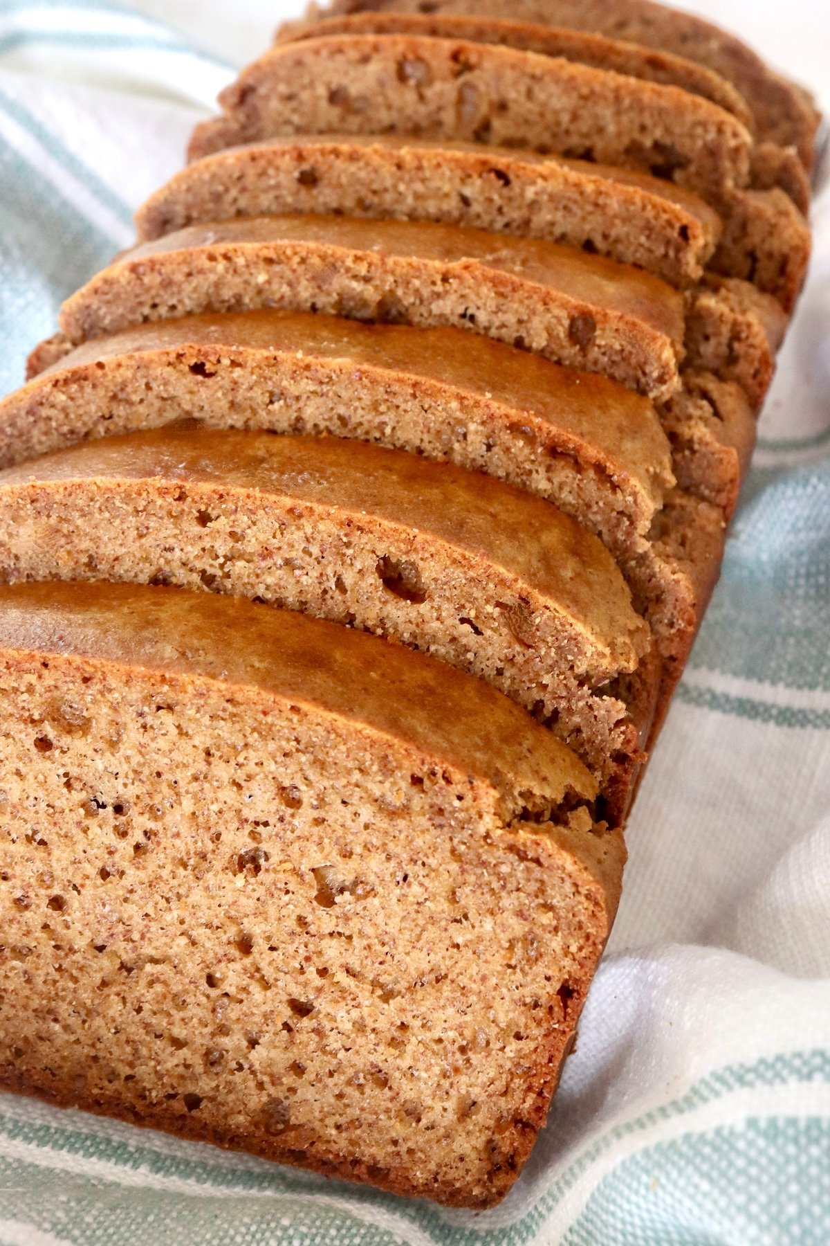 Slices golden loaf of almond butter bread in a cream-colored cloth with a light green strips.