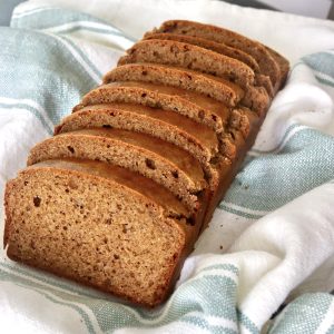 Slices golden loaf of almond butter bread in a cream-colored cloth with a light green strips.