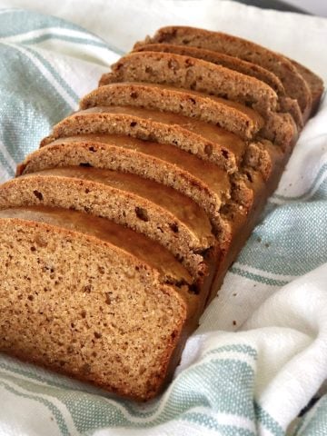 Slices golden loaf of almond butter bread in a cream-colored cloth with a light green strips.