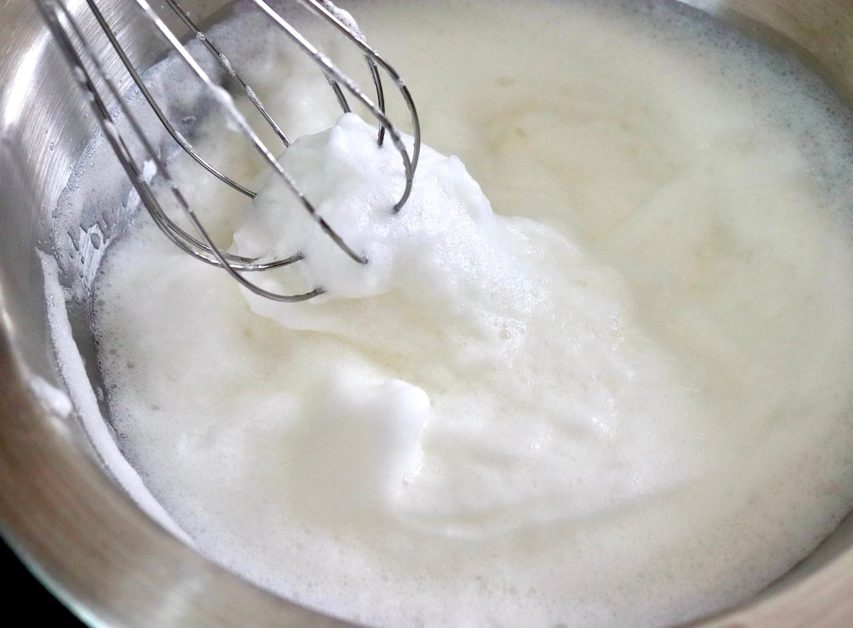 Whipped egg whites in a stainless steel bowl with a whisk.