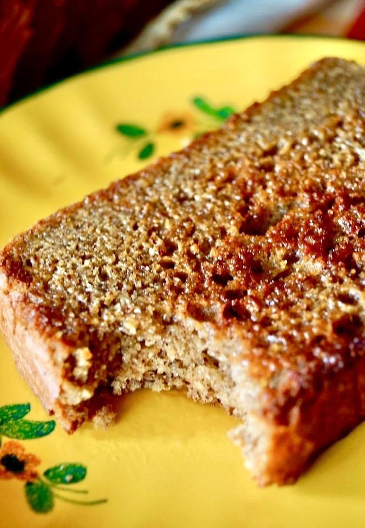 One slice of almond butter bread with a bite taken out of it, on a golden yellow ceramic plate.