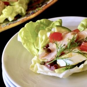 Three stacked white plates with a nicoise sala cup on top with a dill sprig.