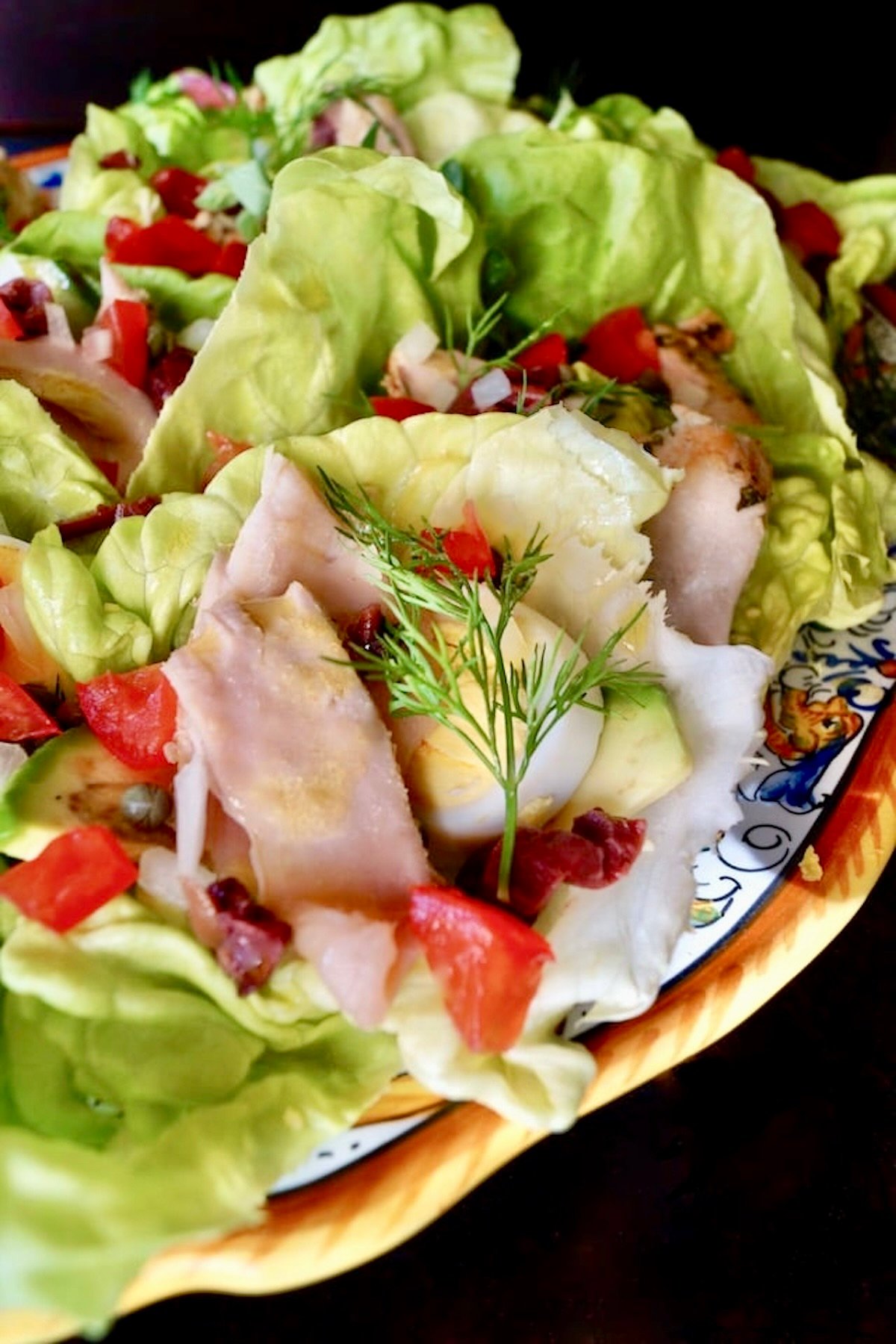 Nicoise Salad Cups Italian painted plate with about a dozen small butter lettuce cups, filled with tuna, egg, tomatoe and olives.