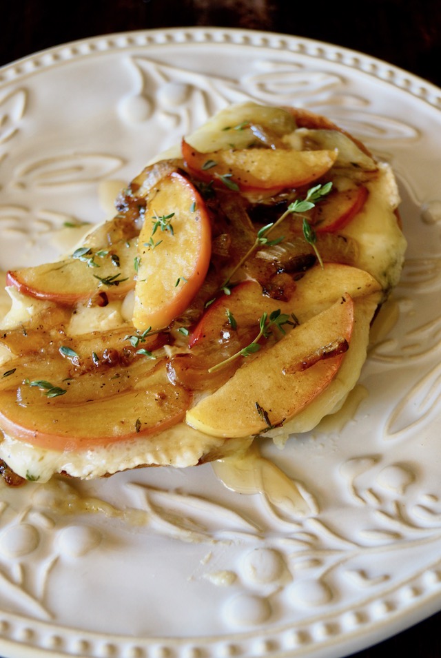 white patterned plate with bread, melting brie cheese, apple slices and sprig of thyme