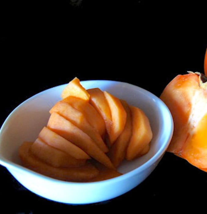 Bright white bowl with wedges of peeled persimmon.