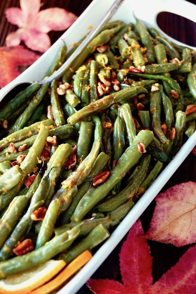 green beans with pecan pieces in white serving dish with red maple leaves in background