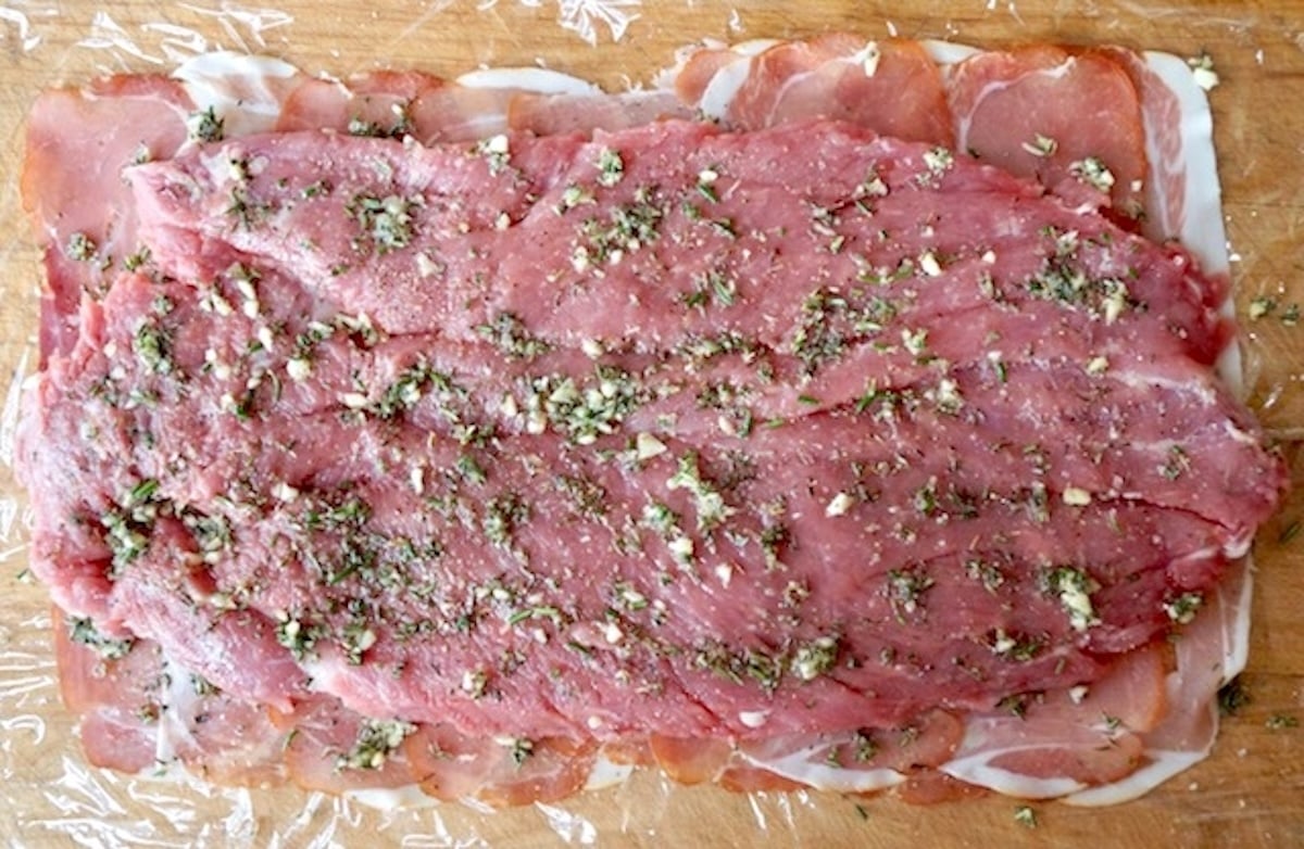 Layer of thin prosciutto slices to form a rectangle, with a butterflied pork tenderloin on top, sprinkled with fresh herbs.
