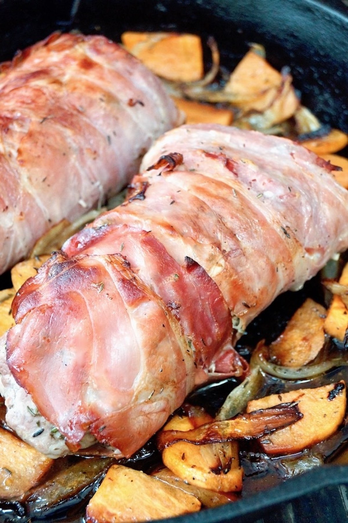 Rolled prosciutto wrapped pork with sliced persimmons inside in a cast iron skillet.
