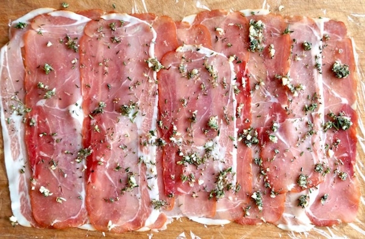 Layer of thin prosciutto slices to form a rectangle, sprinkled with fresh herbs, on plastic wrap.