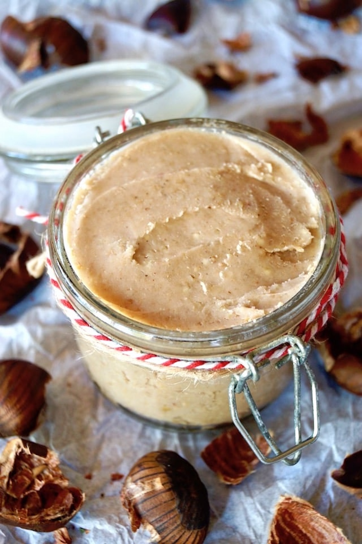 Chestnut butter in a jar with red and white twine around it, surrounded by fresh chestnuts.