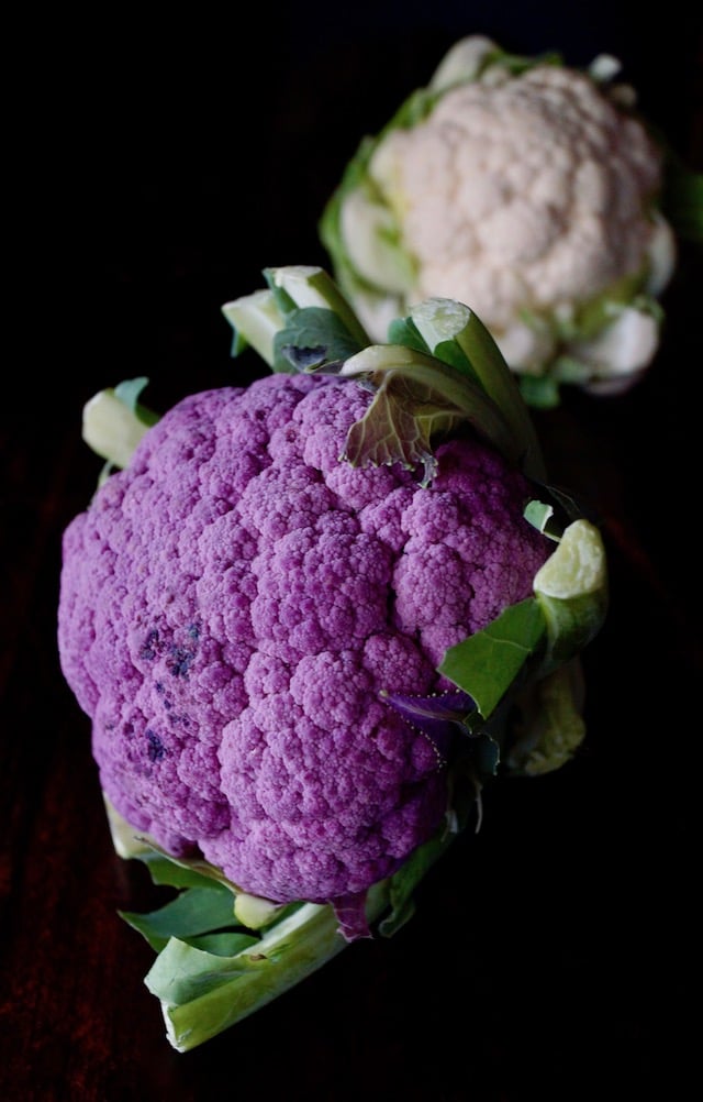 raw purple cauliflower with small white, raw cauliflower in background