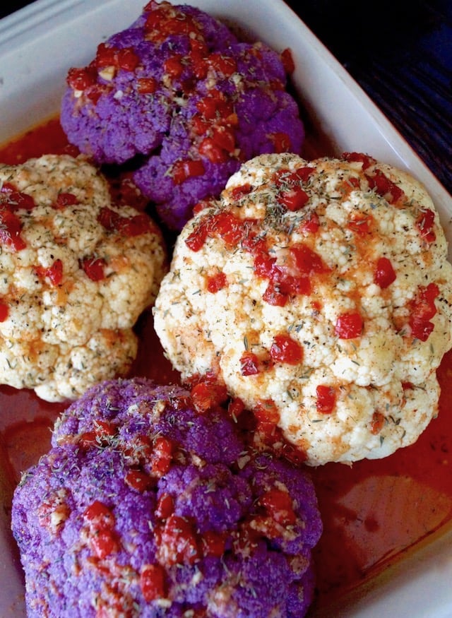 2 purple and 2 whtie raw cauliflower surround by light red sacue and topped with bits of red pepper, in a baking dish