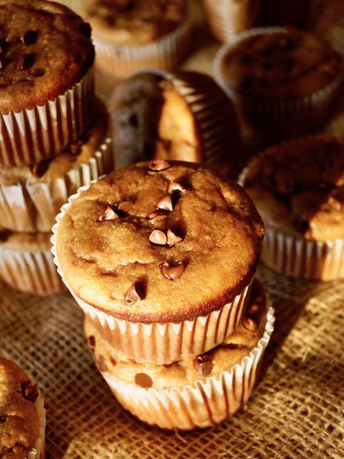 A couple of stacks of banana peanut butter chocolate chip muffins on burlap in pretty light.