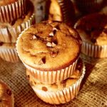 Stack of 2, and stack of 3 gluten-free peanut butter banana muffins with mini chocolate chips, with a few more muffins int he background, on burlap, in the sunlight.