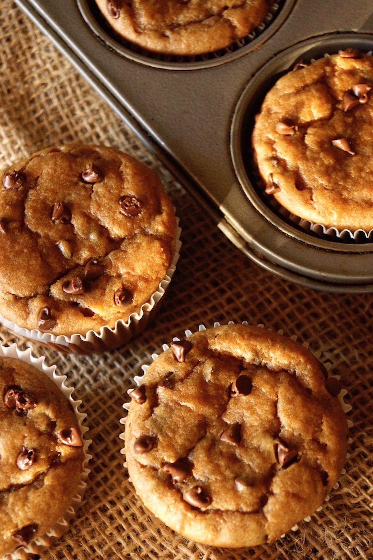 Peanut butter banana Muffins in the pan with a couple of them on burlap right next to it.