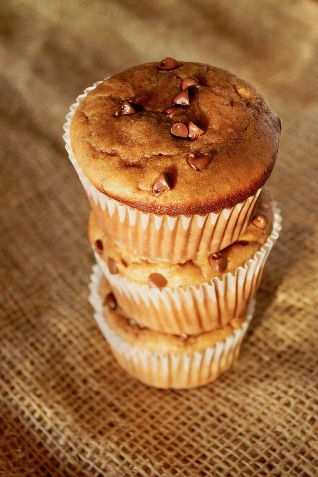 Stack of 3 gluten-free peanut butter banana muffins with mini chocolate chips, on a burlap background.