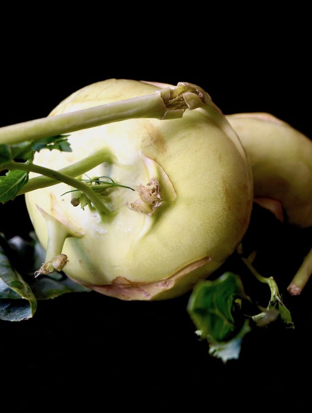 Raw, whole Kohlrabi on its side with stems and leaves for Roasted Kohlrabi.