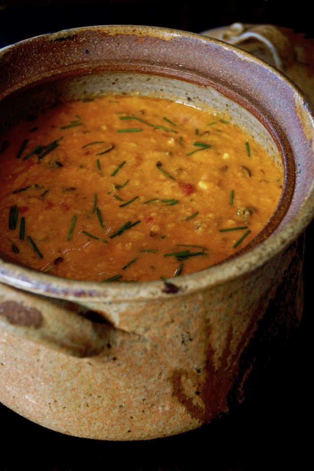 large beige ceramic pot with handles is filled with a melted cheese mixture with chives on top