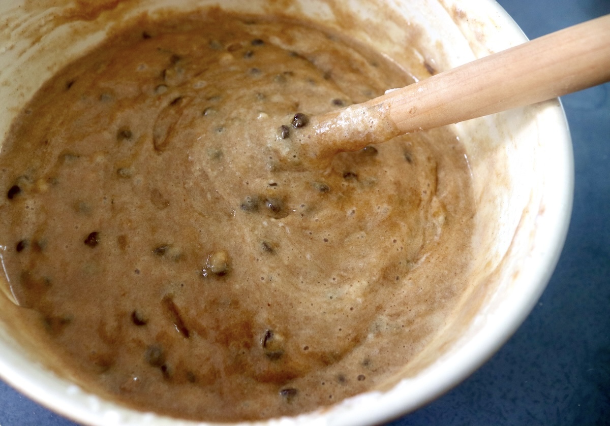 Chocolate chip banana peanut butter muffin batter in a mixing bowl with a wooden spoon.