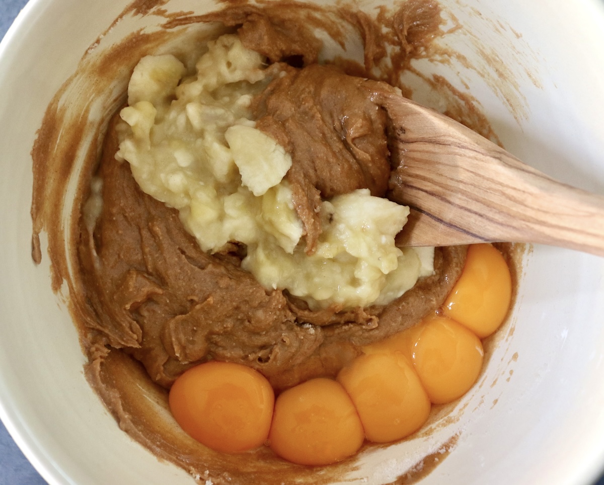 Mashed bananas, egg yolks, and peanut butter in a large mixing bowl with a wooden spoon.