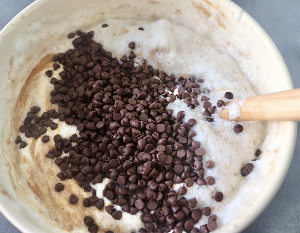 Stiff egg whites and mini chocolate chips being mixed into banana peanut butter muffin batter.