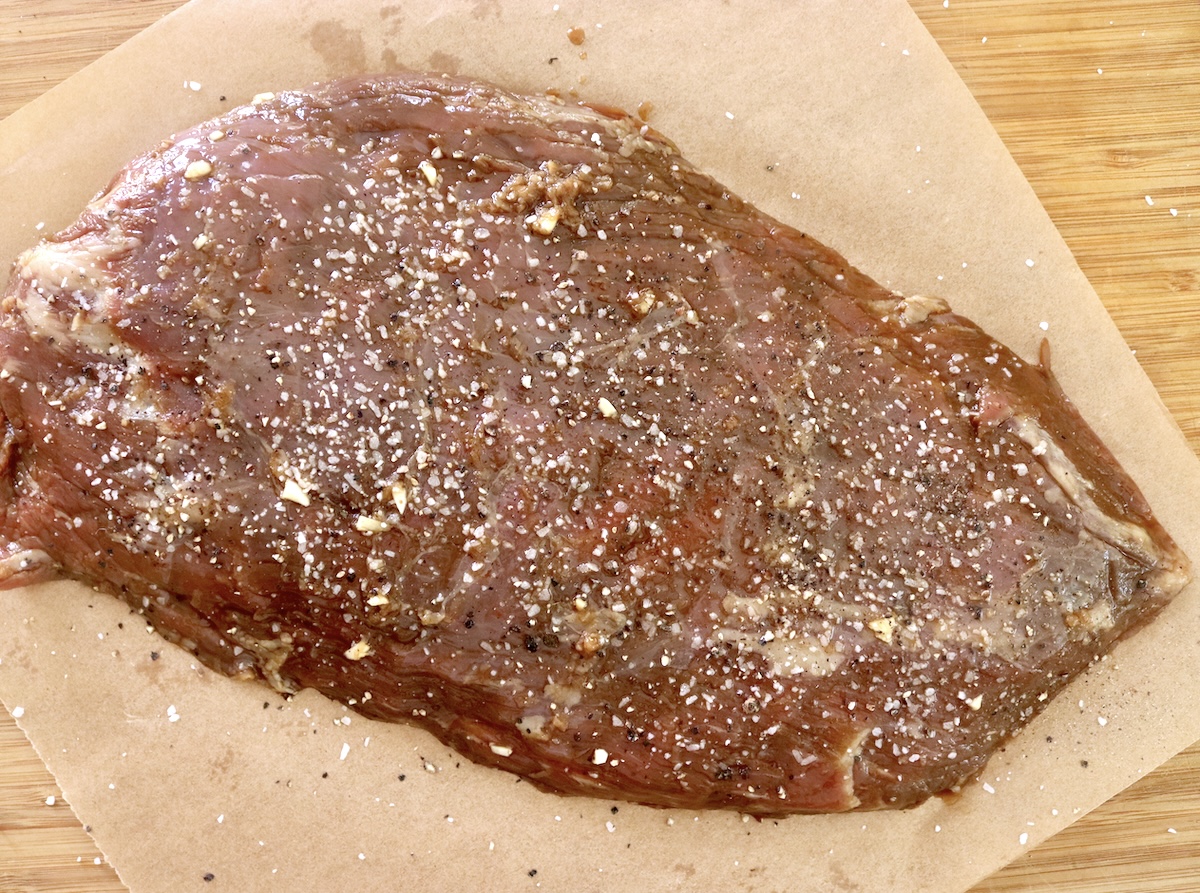 Raw flank steak that's dark from coffee marinade, salted and peppered.