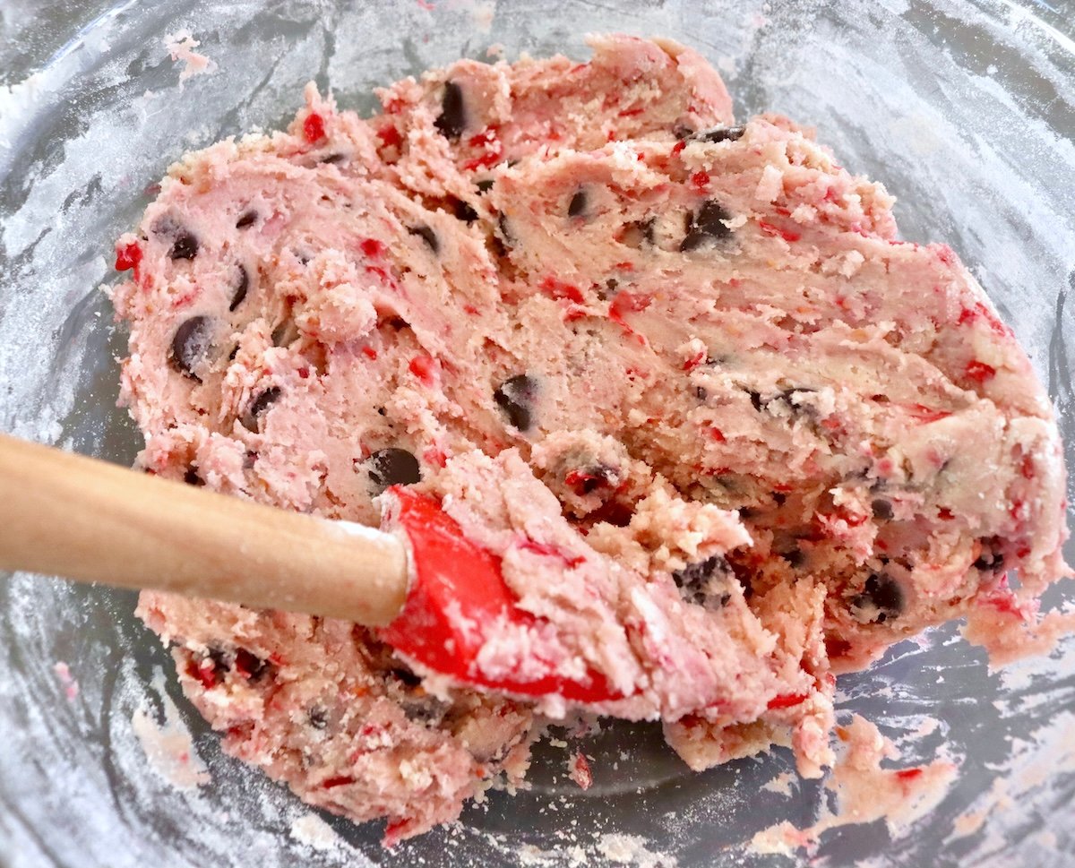 Raspberry-Chocolate-Chip-Cookies Raspberry chocolate chip cookie dough in a glass bowl with a red, wood-handled spatula.