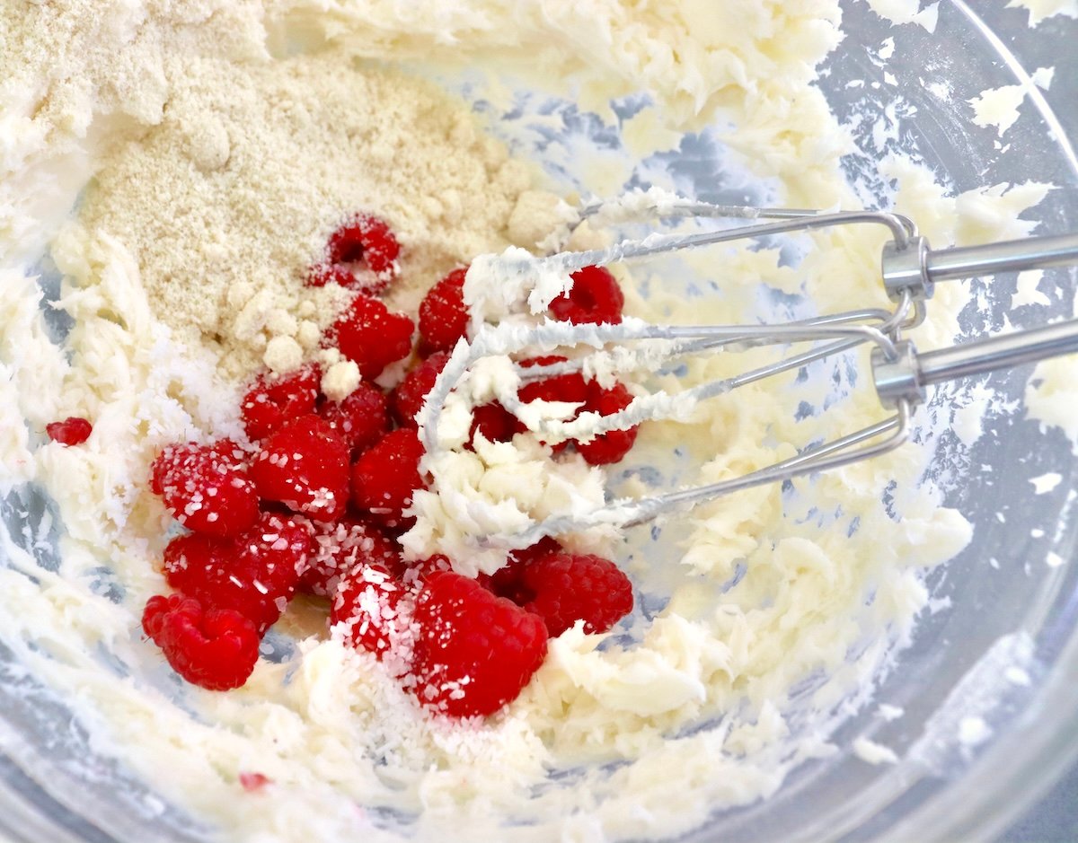Raspberry-Chocolate-Chip-Cookies Butter and sugar mixed together in a glass bowl with fresh raspberries on top, and two beaters from an electric mixer.