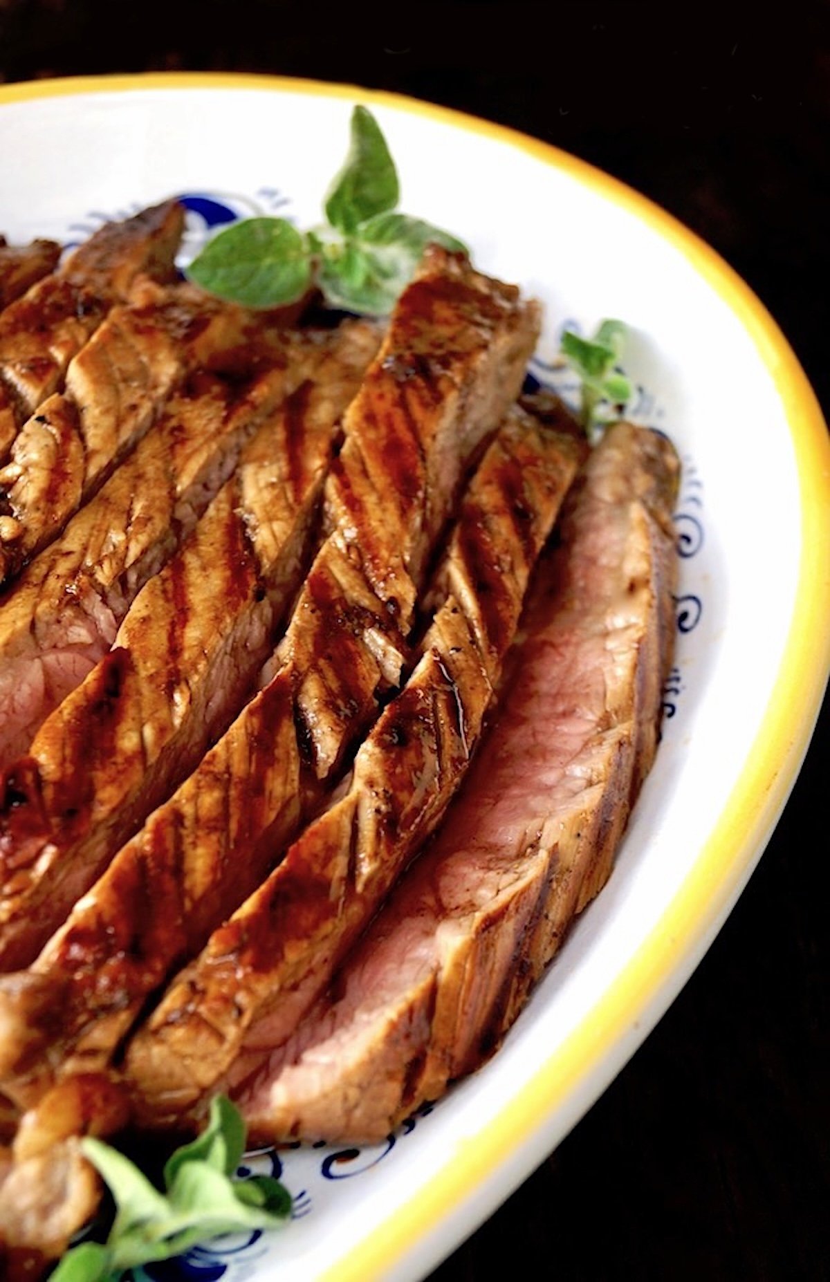 Thinly sliced coffee marinated flank steak on a white serving plate with yellow rim.