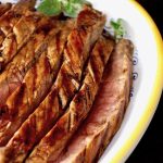 Large yellow-rimmed white platter filled with slices or grilled coffee balsamic flank steak.