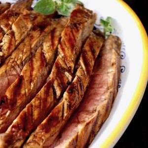 Large yellow-rimmed white platter filled with slices or grilled coffee balsamic flank steak.