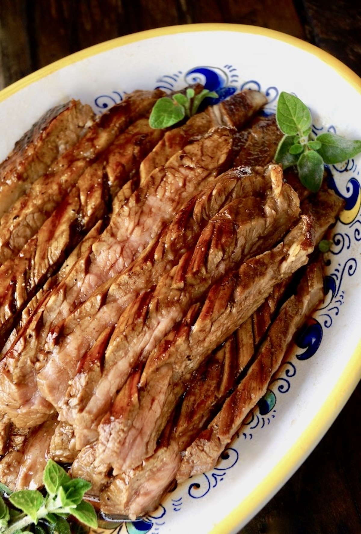 Close up of thinly sliced coffee marinated flank steak on a white serving plate with yellow rim.