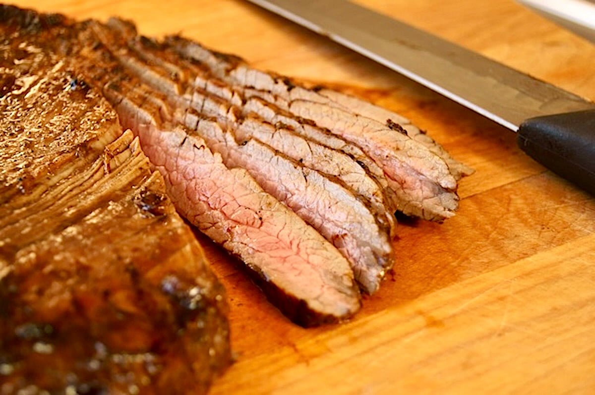 Flank steak slicked thinly against the grain on a cutting board.