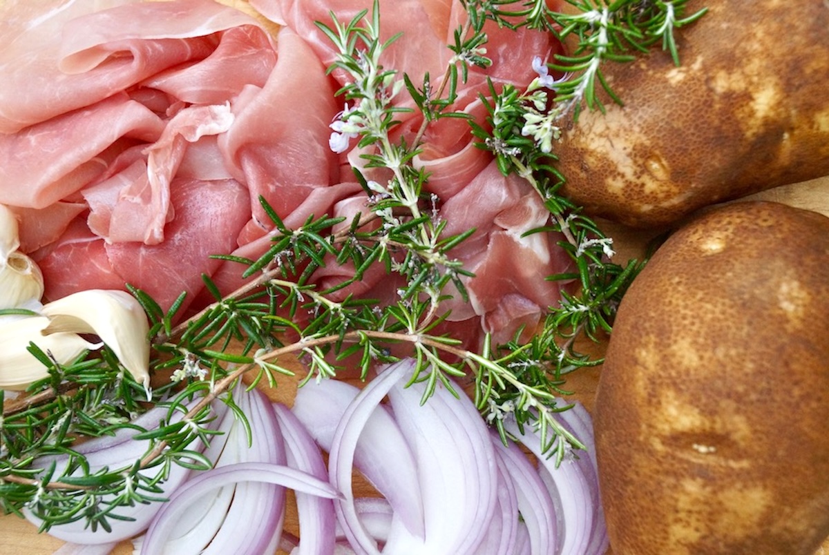Ingredients for Rosemary Prosciutto Cheesy Idaho® Potatoes  including prosciutto, sliced red onion, russet potatoes and fresh sprigs of rosemary