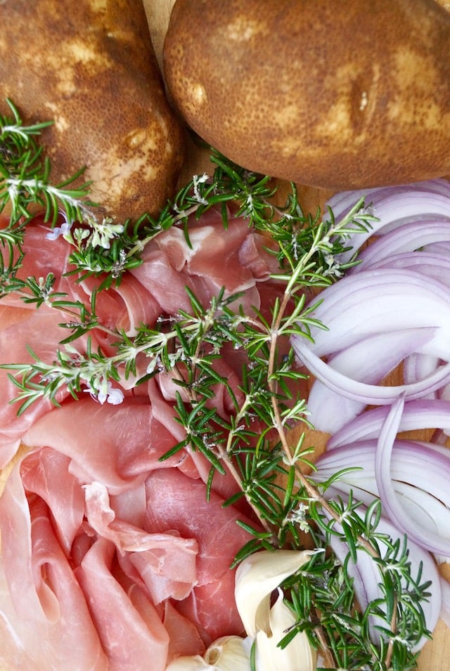 Display of ingredients -- prosciutto, slices of raw onion, fresh rosemary sprigs and two Idaho potatoes.