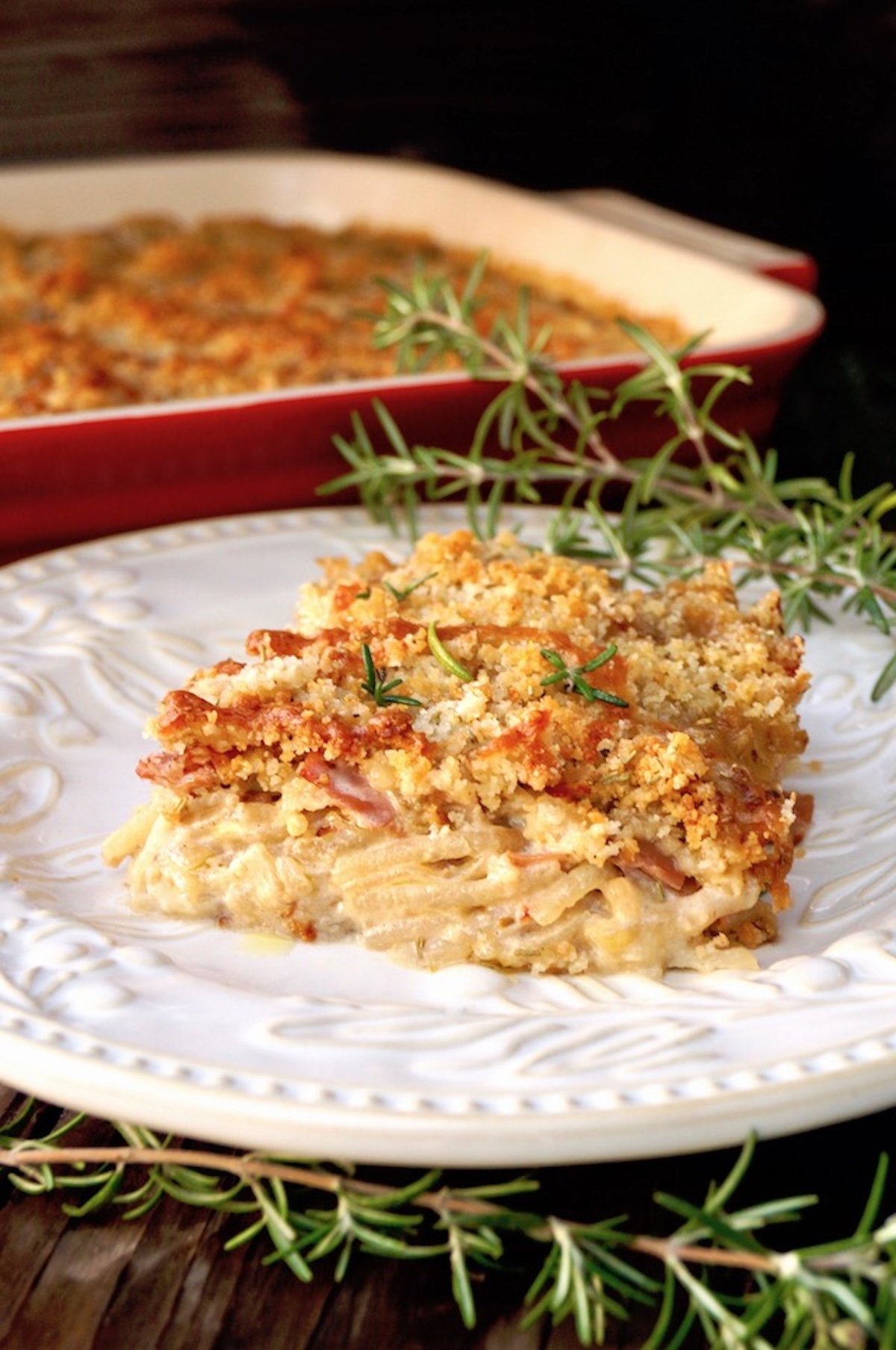 One square of Funeral potatoes (Rosemary Prosciutto Cheesy Idaho® Potatoes) on a white plate with fresh rosemary.