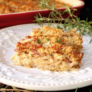 One square of Funeral potatoes (Rosemary Prosciutto Cheesy Idaho® Potatoes) on a white plate with fresh rosemary.