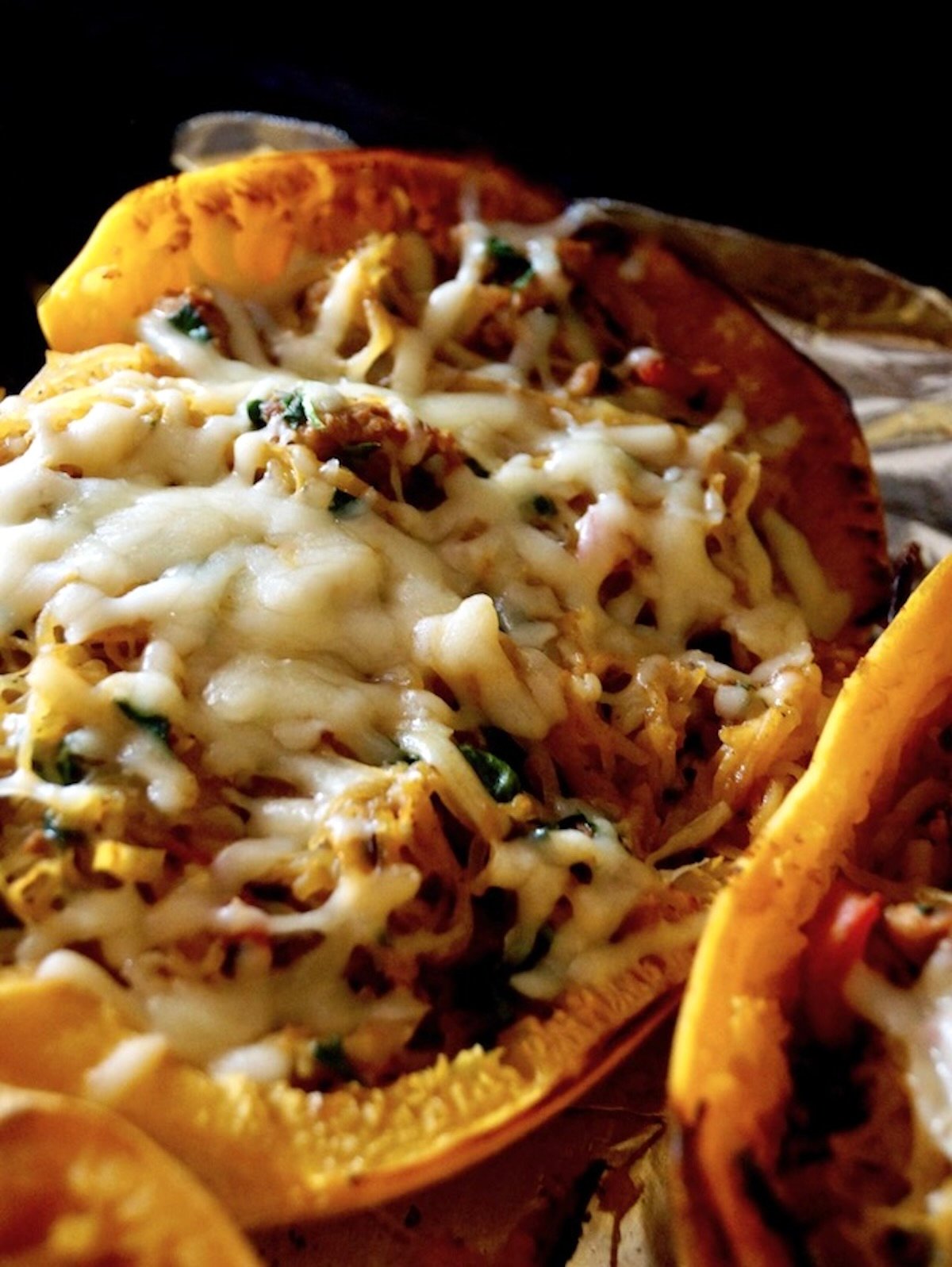 2 spaghetti squash halves filled with squash, sausage and spinach, with melted cheese on top,