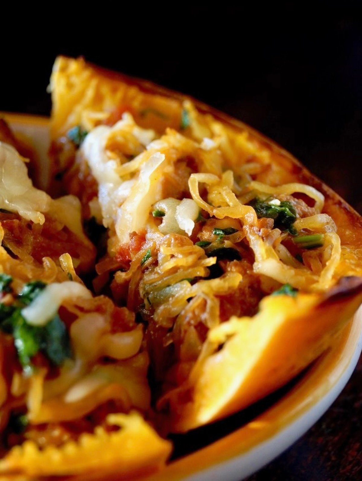 Stuffed spaghetti squash cut into wedges with black background.