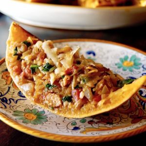 One wedge of spaghetti squash filled with squash, sausage and spinach mixture, with melted cheese on top, on an Italian painted plate.