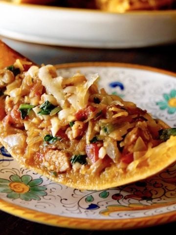 One wedge of spaghetti squash filled with squash, sausage and spinach mixture, with melted cheese on top, on an Italian painted plate.