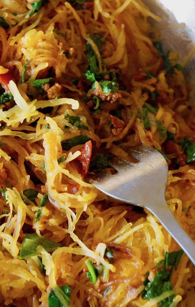 Spaghetti squash mixed with spinach, tomato, sausage and cheese, with a big silver fork.