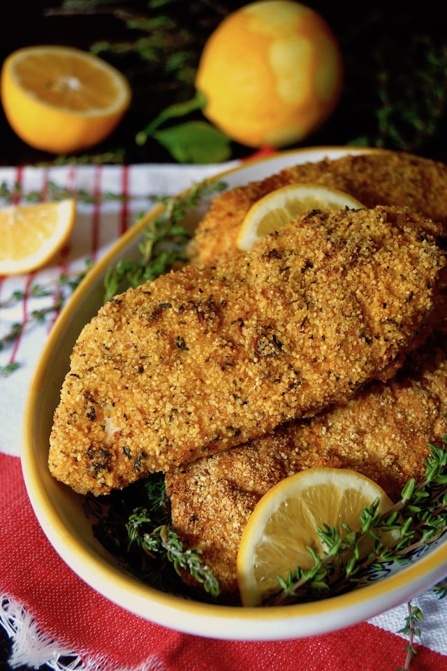 Yellow rimmed bowl full with Air Fryer Gluten-Free Lemon Fried Chicken breasts, with lemons in background.