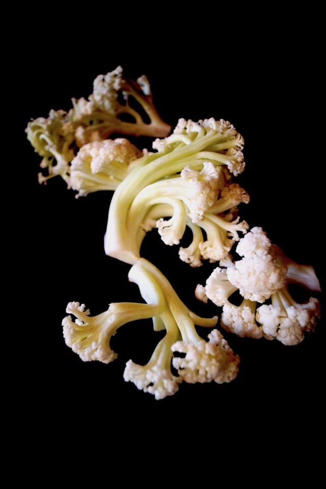 A few pieces of fioretto, flowering cauliflower, n a black background.