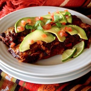 Two enchiladas on a white plate with thinly sliced avocado and diced tomato.