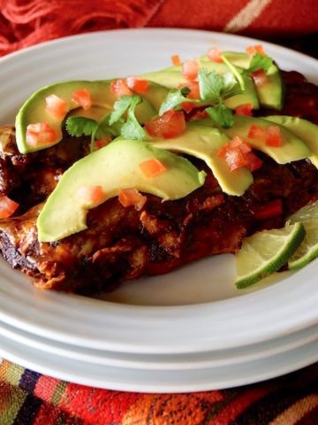 Two enchiladas on a white plate with thinly sliced avocado and diced tomato.